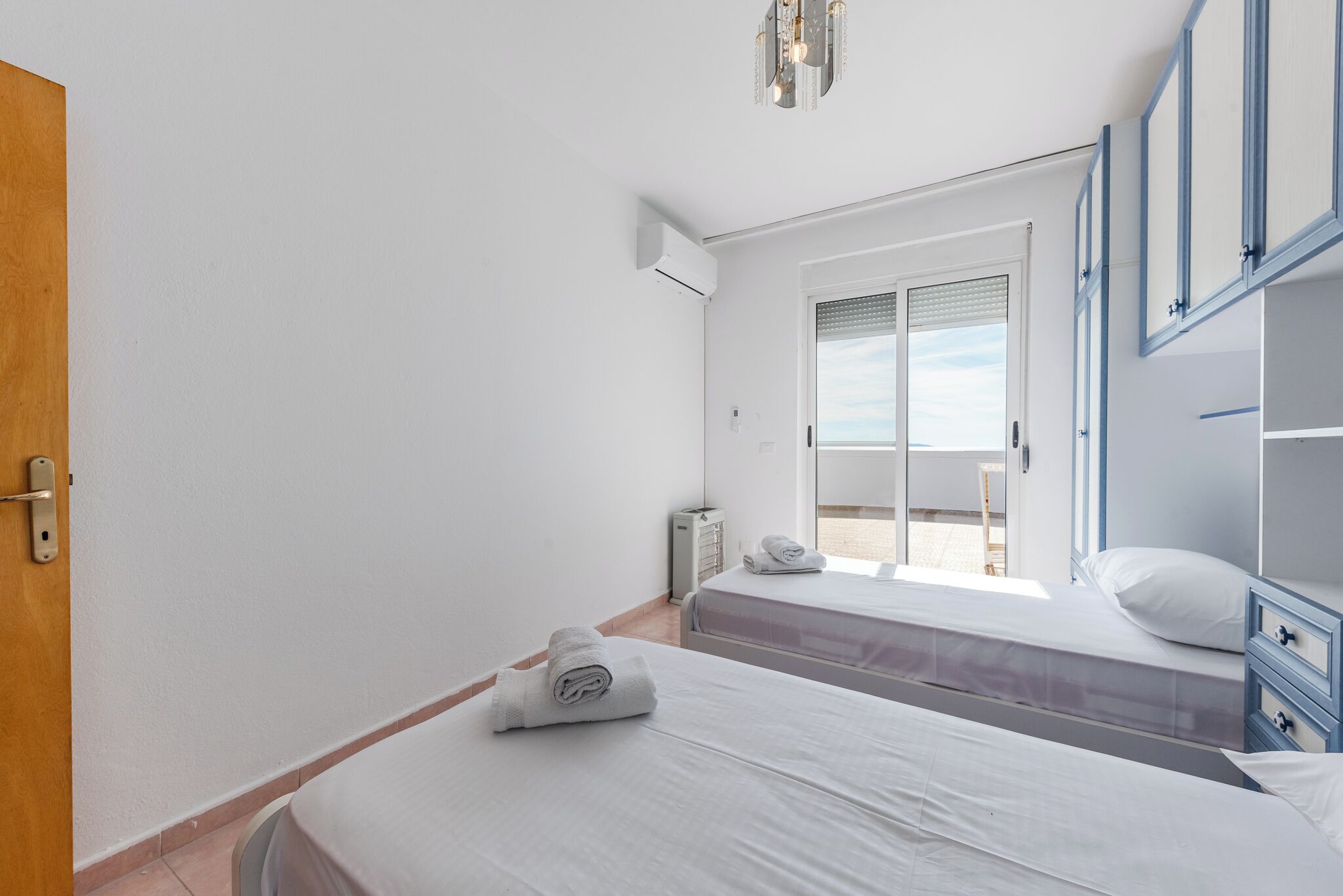 A hotel room with two beds, a window with blinds, a ceiling light fixture, and a door.
