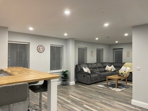 A modern living room with a grey sofa, a wooden coffee table, and a dining area with a wooden table and bar stools. - Spacious 5Br Home - Country View - Close to Galway (Tuam)
