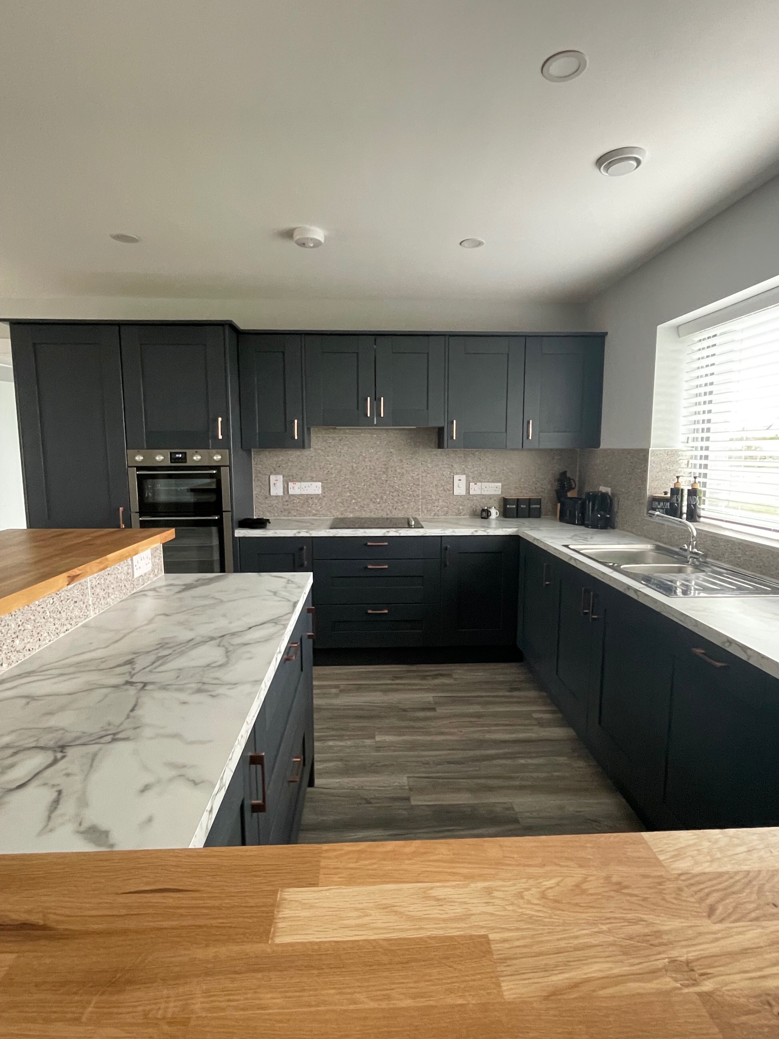 A modern kitchen with dark cabinets, a marble countertop, and a built-in oven.