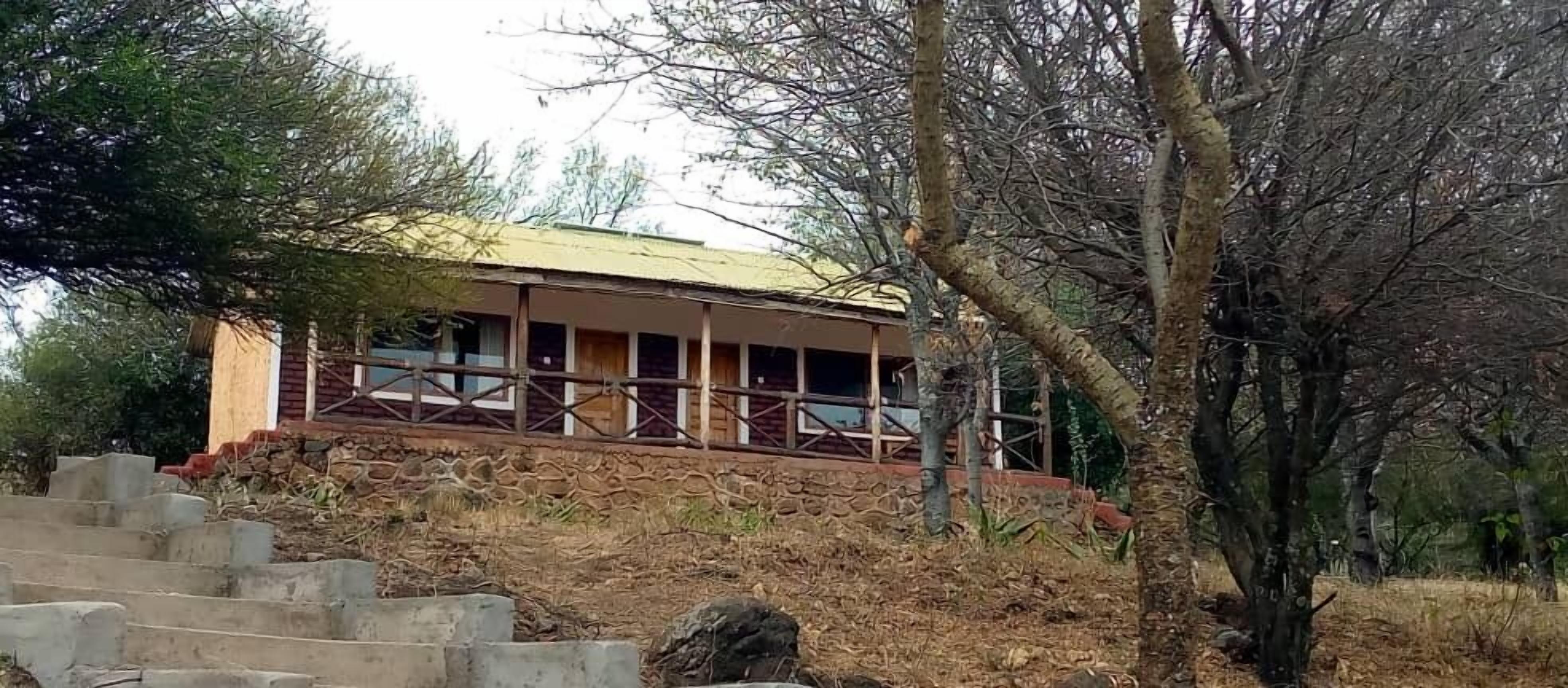 A rustic building with a wooden exterior and a balcony, surrounded by trees and a stone staircase.