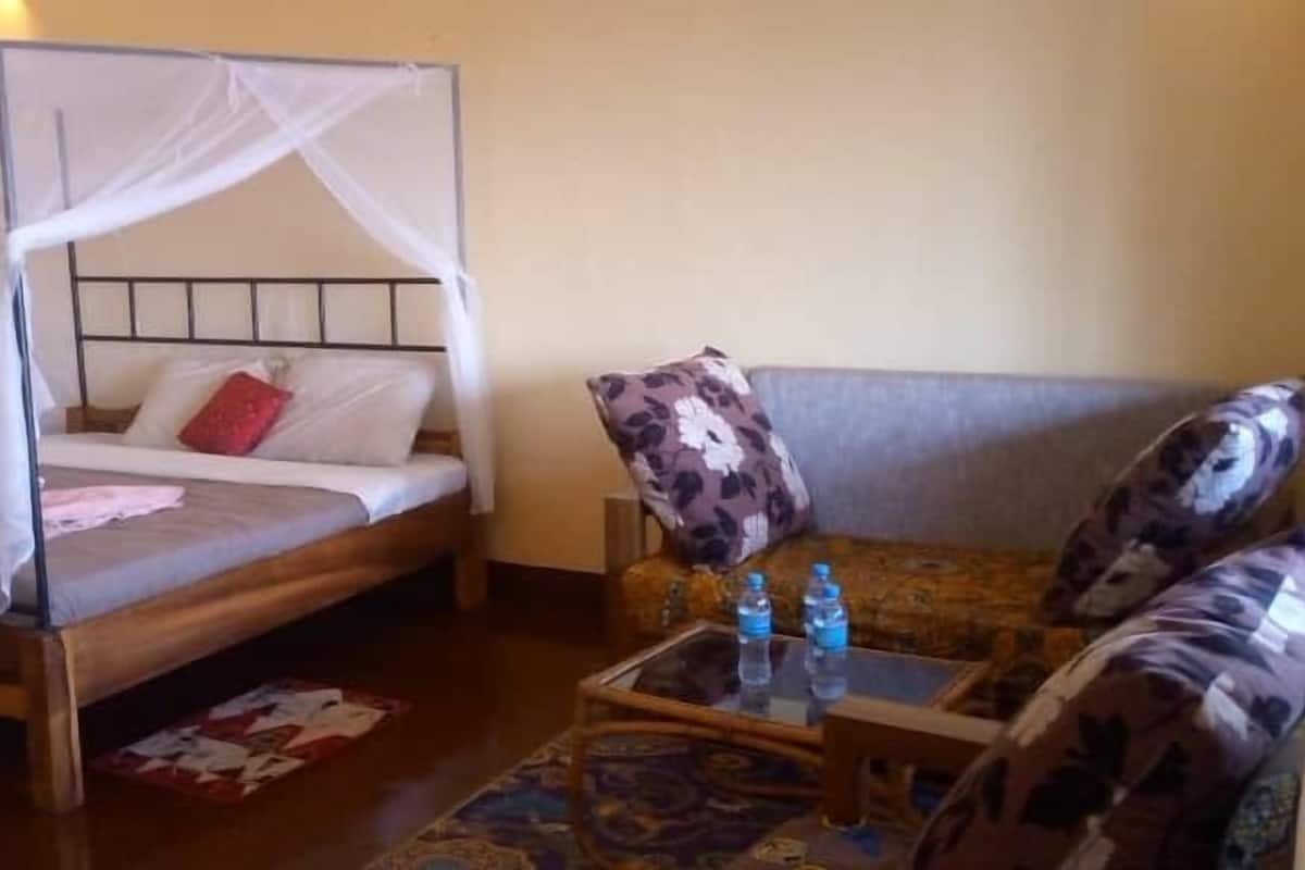 Une chambre avec un lit recouvert d’une moustiquaire, un canapé et une petite table sur laquelle se trouvent des bouteilles d’eau.