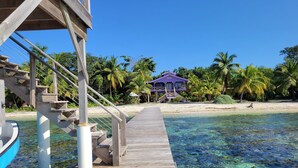 A wooden pier leading to a beach with clear water, a purple building, and palm trees. - Lavender House at Treasure Beach - Secluded Beach House (Bay Islands Department)
