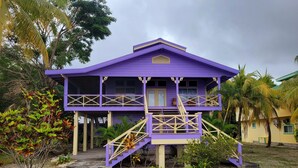 A two-story building with a purple exterior, a balcony on the upper floor, and a staircase leading to the entrance. - Lavender House at Treasure Beach - Secluded Beach House (Bay Islands Department)