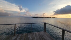 A wooden deck with a railing overlooking a calm sea and a distant island. - Lavender House at Treasure Beach - Secluded Beach House (Bay Islands Department)