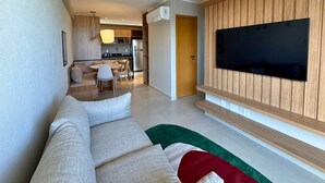 Ein modernes Wohnzimmer mit einer Couch, einem Flachbildfernseher, der an einer Wand aus Holzpaneelen befestigt ist, und einer Küche im Hintergrund.