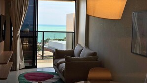 Ein modernes Wohnzimmer mit einer Couch, einem runden Teppich und einem großen Fenster mit Blick auf das Meer.