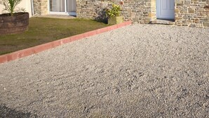 Un bâtiment en pierre avec une allée gravillonnée, une porte bleue et un petit jardin.