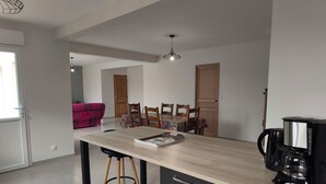 Une cuisine moderne avec un îlot central, des chaises en bois, une machine à café et une table à manger recouverte d’une nappe colorée.