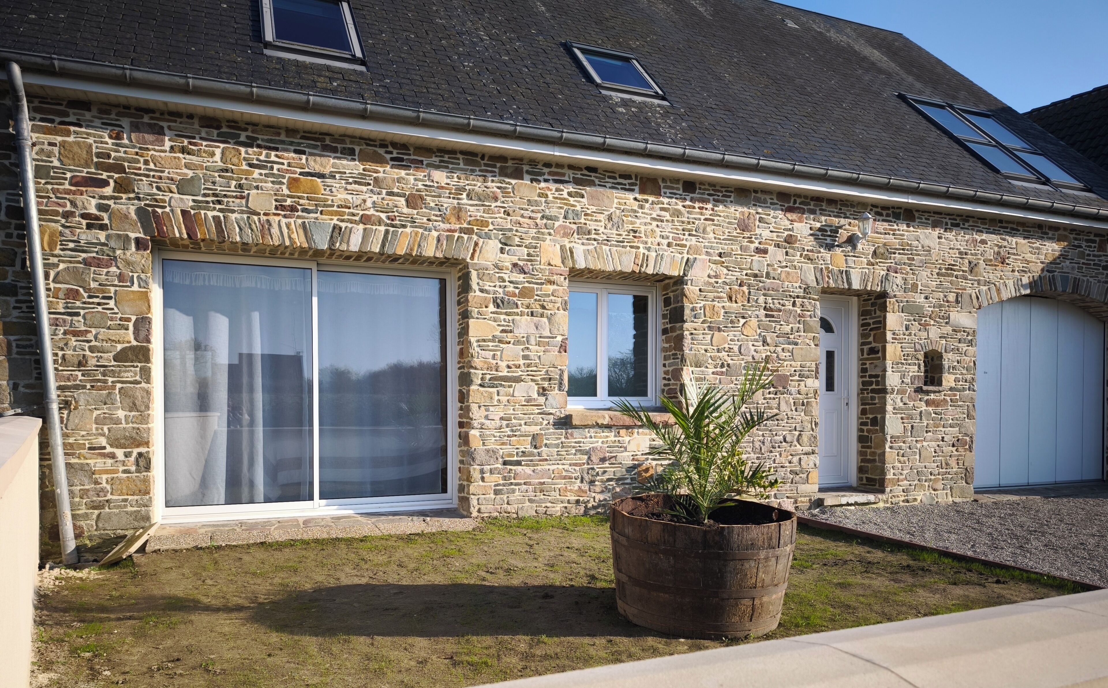 A stone house with large windows, a door, and a small garden area with a potted plant.