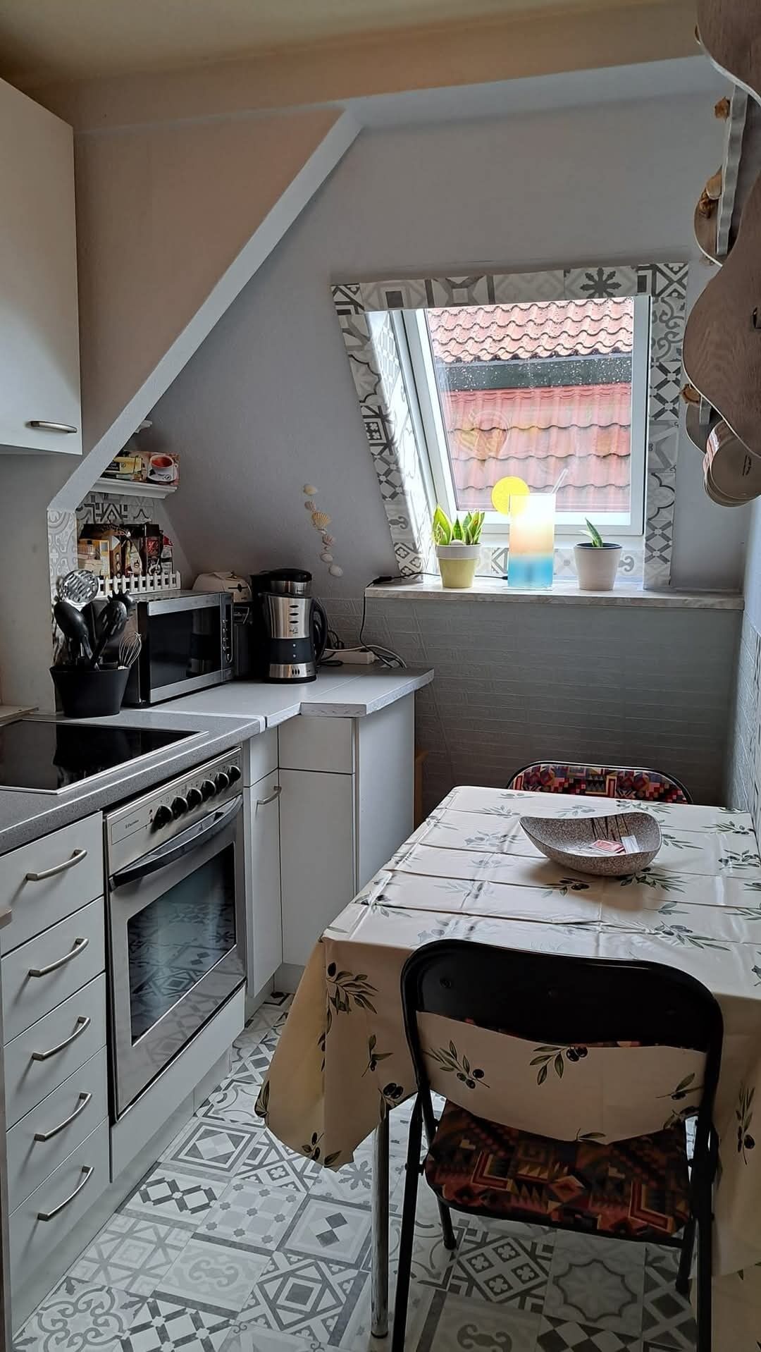 Een kleine keuken met een eettafel, een magnetron, een oven en een raam met planten.