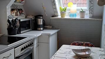 Een kleine keuken met een eettafel, een magnetron, een oven en een raam met planten.