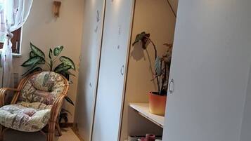 Um quarto com uma cadeira estampada, uma planta em vaso, um guarda-roupa e uma estante com objetos.