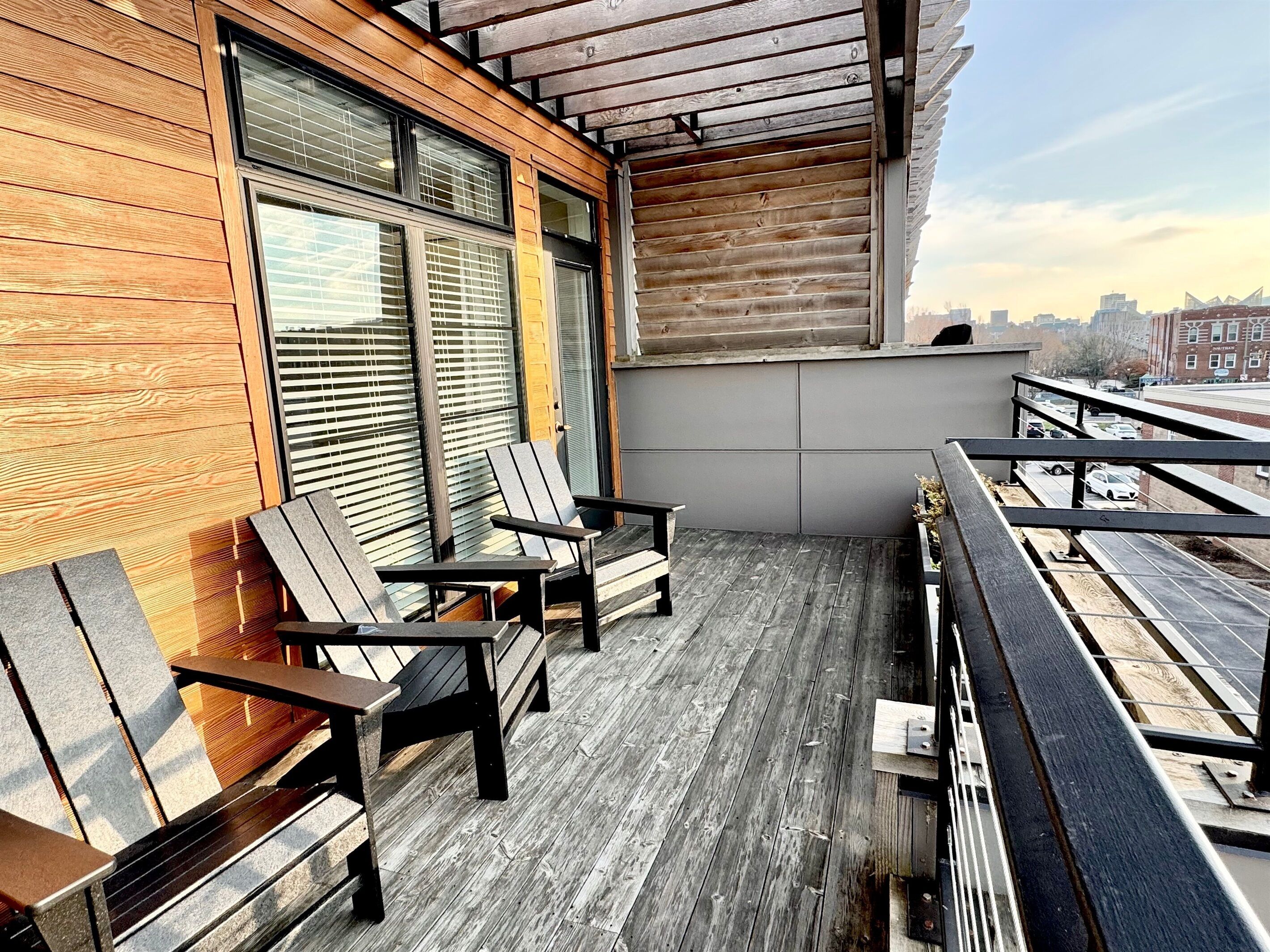 A balcony with wooden flooring and metal railings, featuring two wooden chairs and a table.