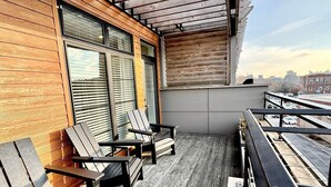A balcony with wooden flooring and metal railings, featuring two wooden chairs and a table.