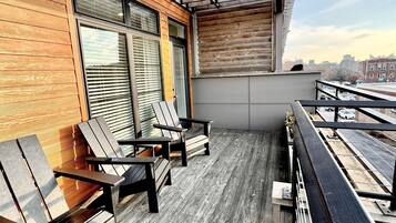 A balcony with wooden flooring and metal railings, featuring two wooden chairs and a table.