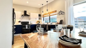 A modern kitchen with white cabinets, a black stove, and a dining area with a wooden table set for four.