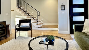 A modern living room with a staircase, a green sofa, a black chair, and a coffee table with a plant.