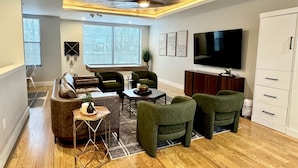 A modern living room with a wooden ceiling, a large TV, and a seating area with a sofa and chairs.