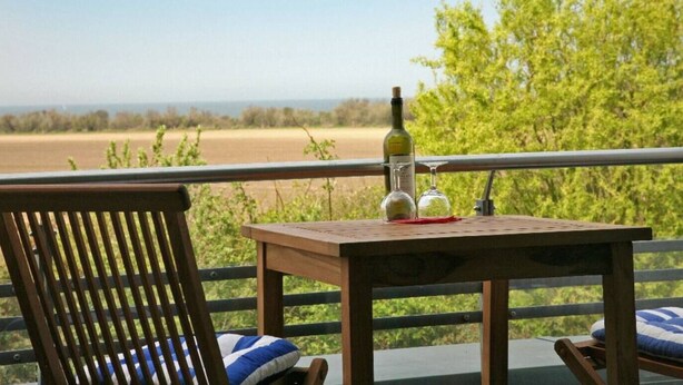 Una mesa de madera con una botella y un vaso en un balcón con vista a un campo y árboles.
