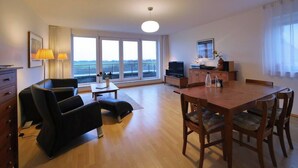 Una sala moderna con una mesa de comedor de madera, un sofá de cuero negro y un televisor.