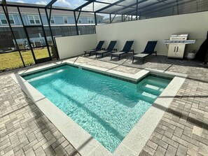 A swimming pool with lounge chairs and a grill area, surrounded by a glass enclosure.