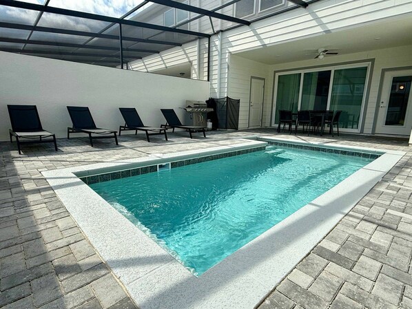 A rectangular indoor pool with a tiled edge, surrounded by lounge chairs and a covered patio area.