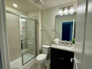 A modern bathroom with a glass-enclosed shower, a white toilet, and a granite countertop sink.