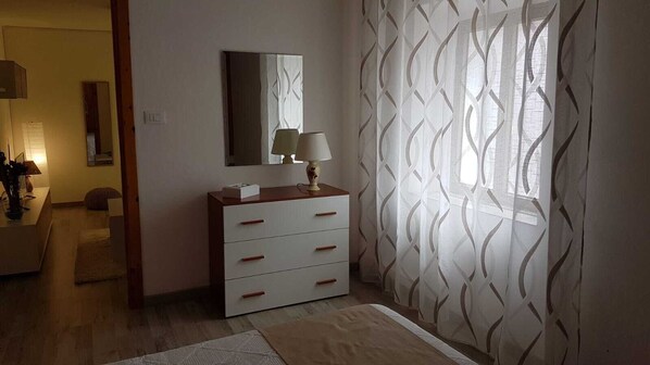 Un dormitorio con un aparador de madera, un espejo y una ventana con cortinas estampadas.