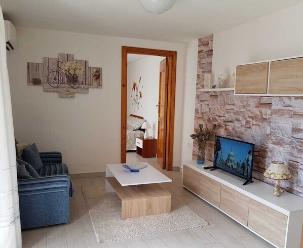 A modern living room with a sofa, coffee table, and TV on a stone wall.