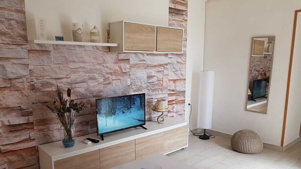A modern living room with a stone wall, a flat-screen TV, a white console table, a blue glass bowl, and a mirror.