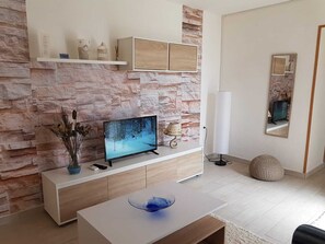 Una sala de estar moderna con pared de piedra, televisor de pantalla plana, consola blanca, cuenco de vidrio azul y un espejo.