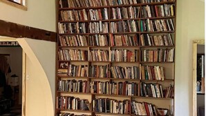 Una habitación con una amplia estantería llena de libros, un banco de madera y un extintor.
