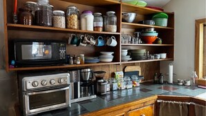 Una cocina con microondas, horno y varios utensilios y electrodomésticos de cocina sobre estantes de madera.