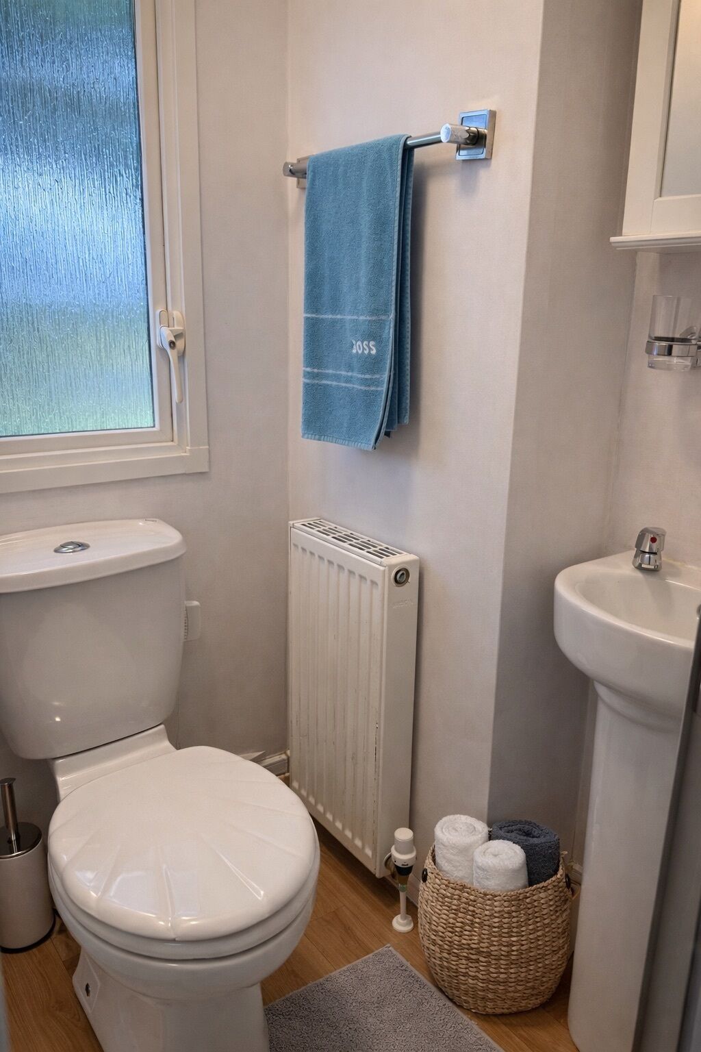 Een badkamer met toilet, radiator, handdoekrek met een blauwe handdoek, wastafel en een mand met handdoeken.