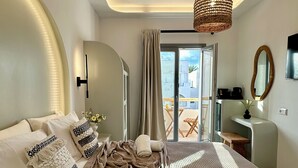 A modern bedroom with a large bed, a curved wall, a ceiling light, and a view of the outside. - Marjay (Paros)