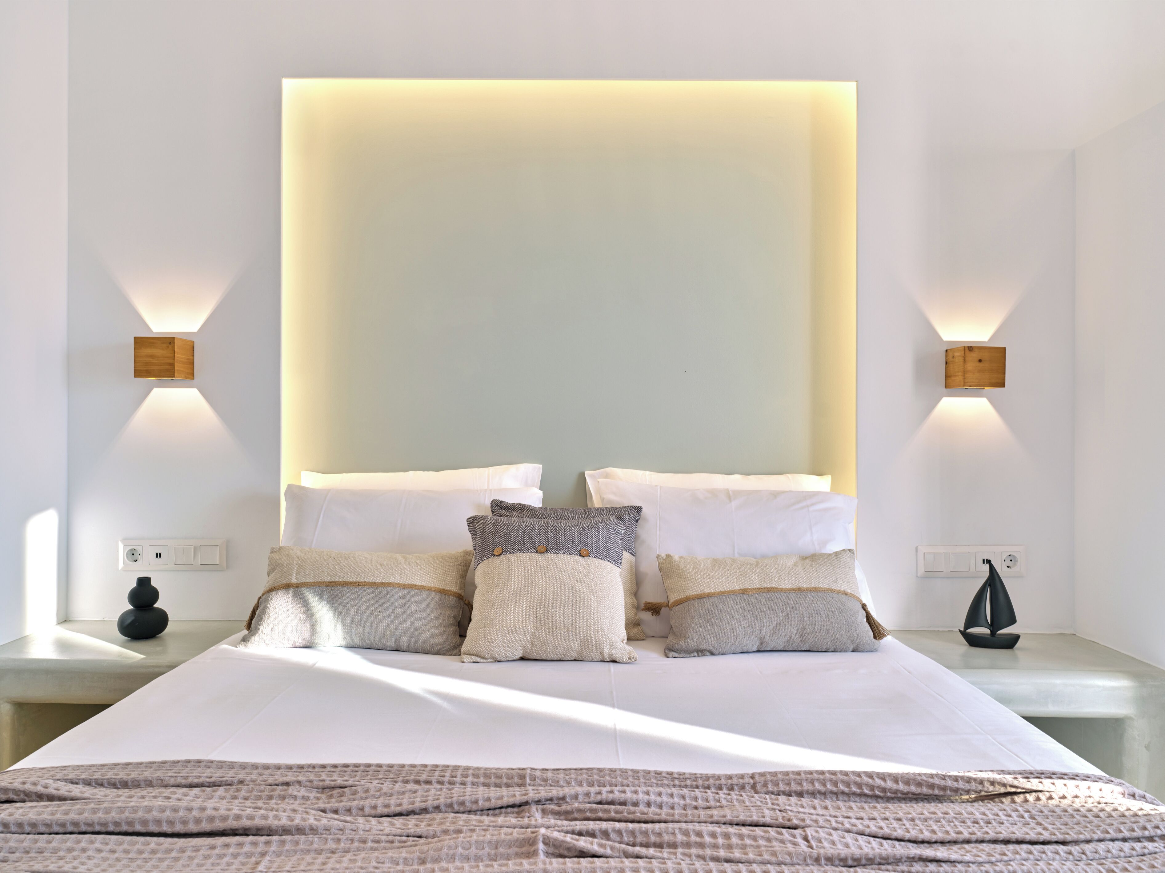 A modern bedroom with a large bed, multiple pillows, bedside tables, and wall-mounted lighting.