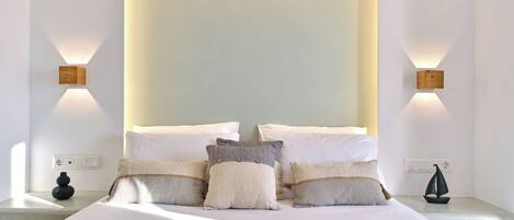 A modern bedroom with a large bed, multiple pillows, bedside tables, and wall-mounted lighting.