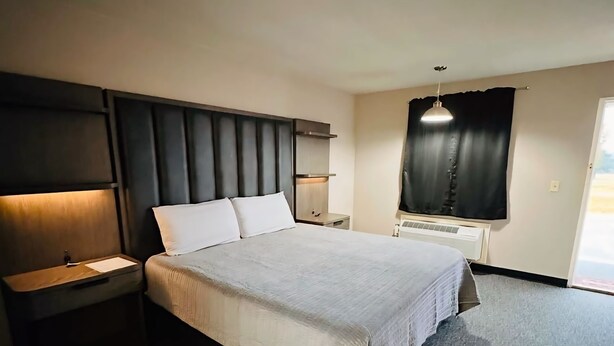 A modern hotel room with a large bed, a bedside table, a nightstand, a wall-mounted shelf, and a window with curtains. - DeQueen Golf and Country Club (De Queen)