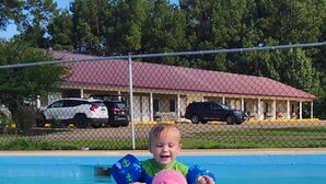 A child in a swimming pool with a pink swim cap and blue arm floaties, holding a pink cap. - DeQueen Golf and Country Club (De Queen)