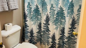 A bathroom with a toilet, a roll of toilet paper, and a shower curtain with a forest pattern. - DeQueen Golf and Country Club (De Queen)