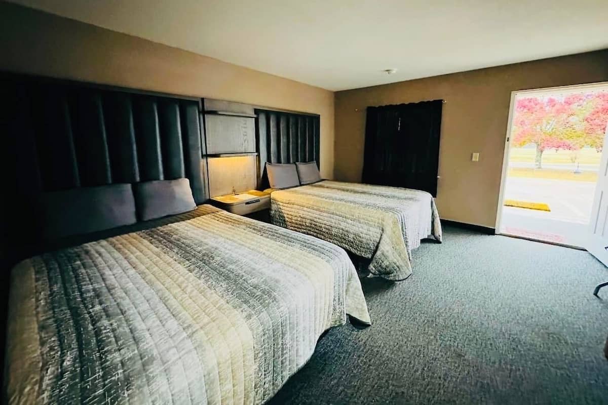 A hotel room with two beds, a headboard, a nightstand, a window with a view, and a door leading outside.