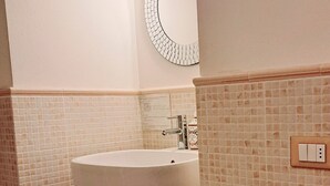 A bathroom with a freestanding bathtub, a wall-mounted light fixture, and a small shelf with toiletries. - Burlamacco Gold modern rooms in the center of Viareggio 350 meters from the Sea (Viareggio)