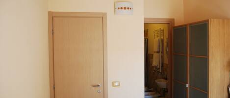 Una habitación con puerta de madera, un baño pequeño con inodoro y lavamanos, y una puerta corredera de vidrio.