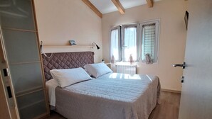 A bedroom with a bed, wooden beams, a window with curtains, and a radiator. - Burlamacco Gold modern rooms in the center of Viareggio 350 meters from the Sea (Viareggio)