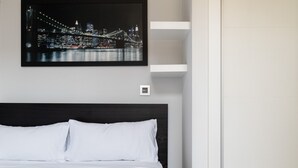 A hotel room with a neatly made bed, a framed cityscape picture on the wall, and a modern headboard.
