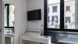 A modern bathroom with a glass shower enclosure, a white sink, and a mounted television.