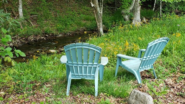 Dos sillas Adirondack azules junto a un arroyo en un área boscosa.