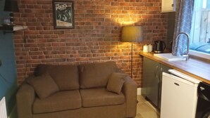 Una cocina con pared de ladrillo, sofá, pileta y refrigerador.