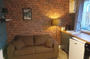 A kitchen with a brick wall, a sofa, a sink, and a refrigerator.