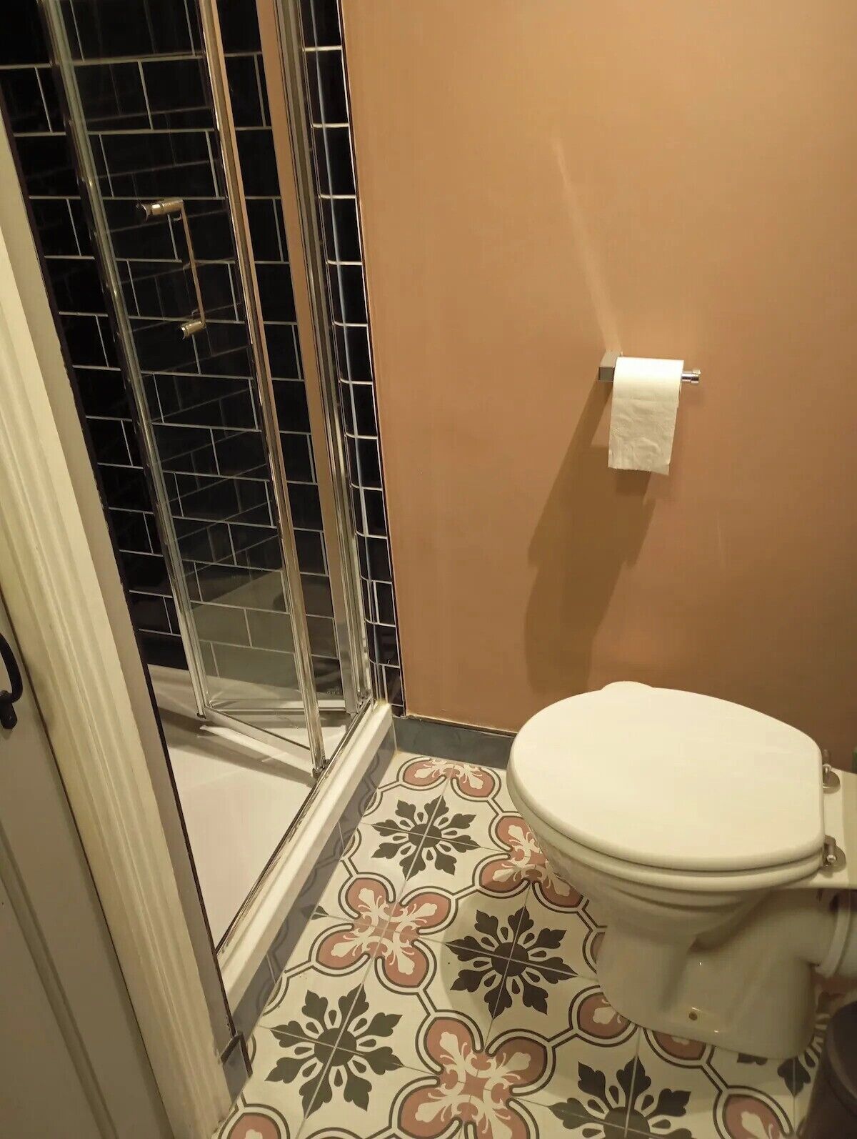A bathroom with a shower, toilet, and patterned floor tiles.